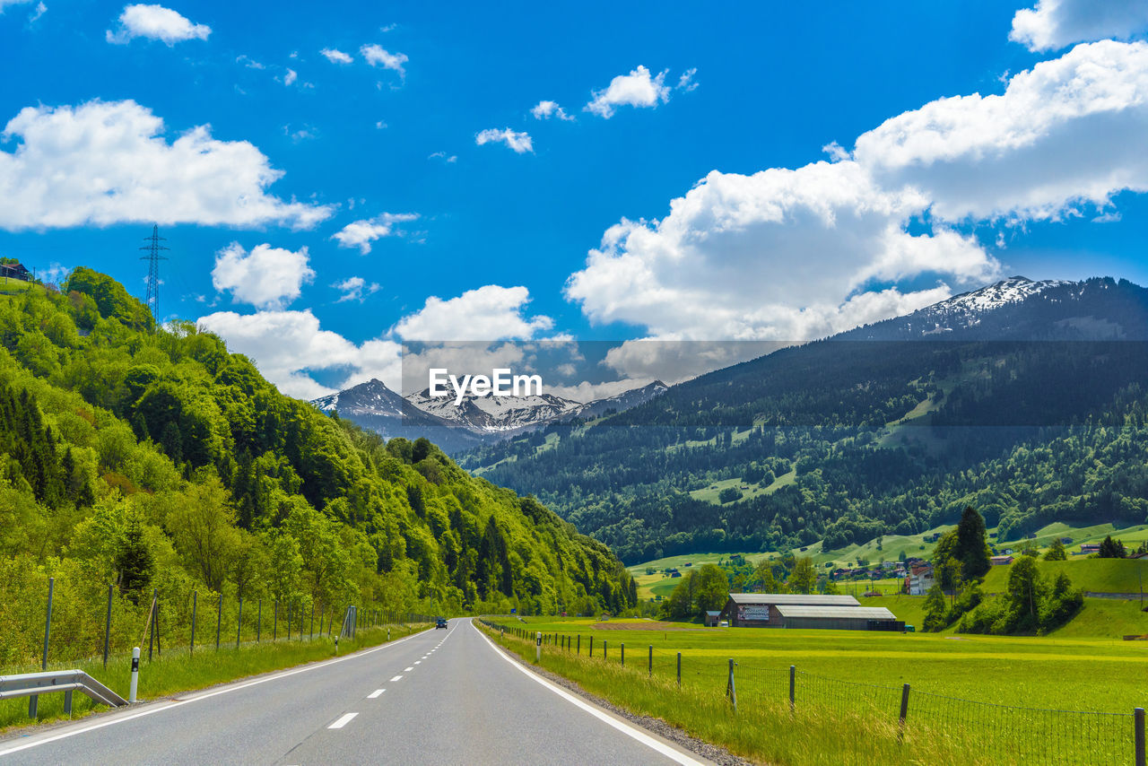 ROAD AMIDST TREES AND LANDSCAPE AGAINST SKY