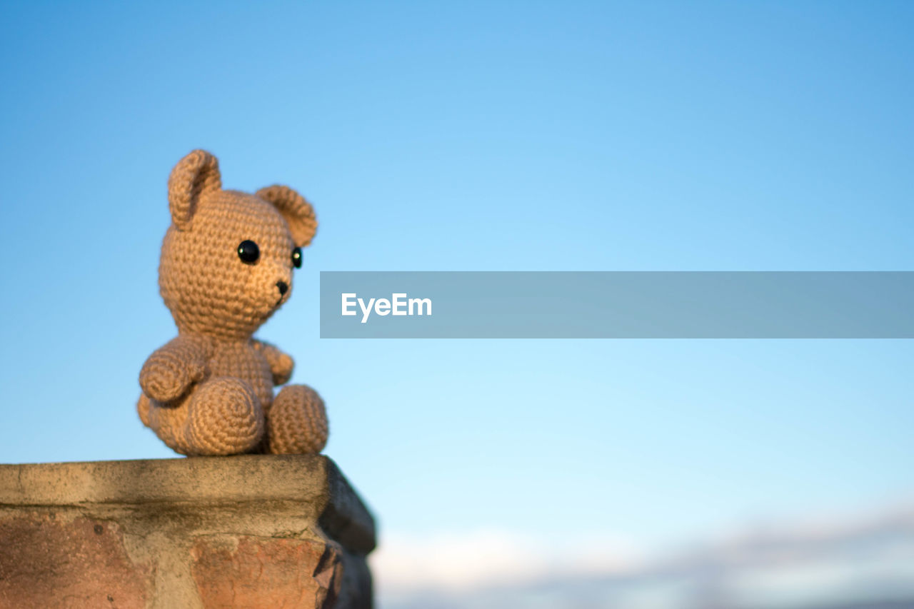 Low angle view of teddy bear on retaining wall against clear blue sky