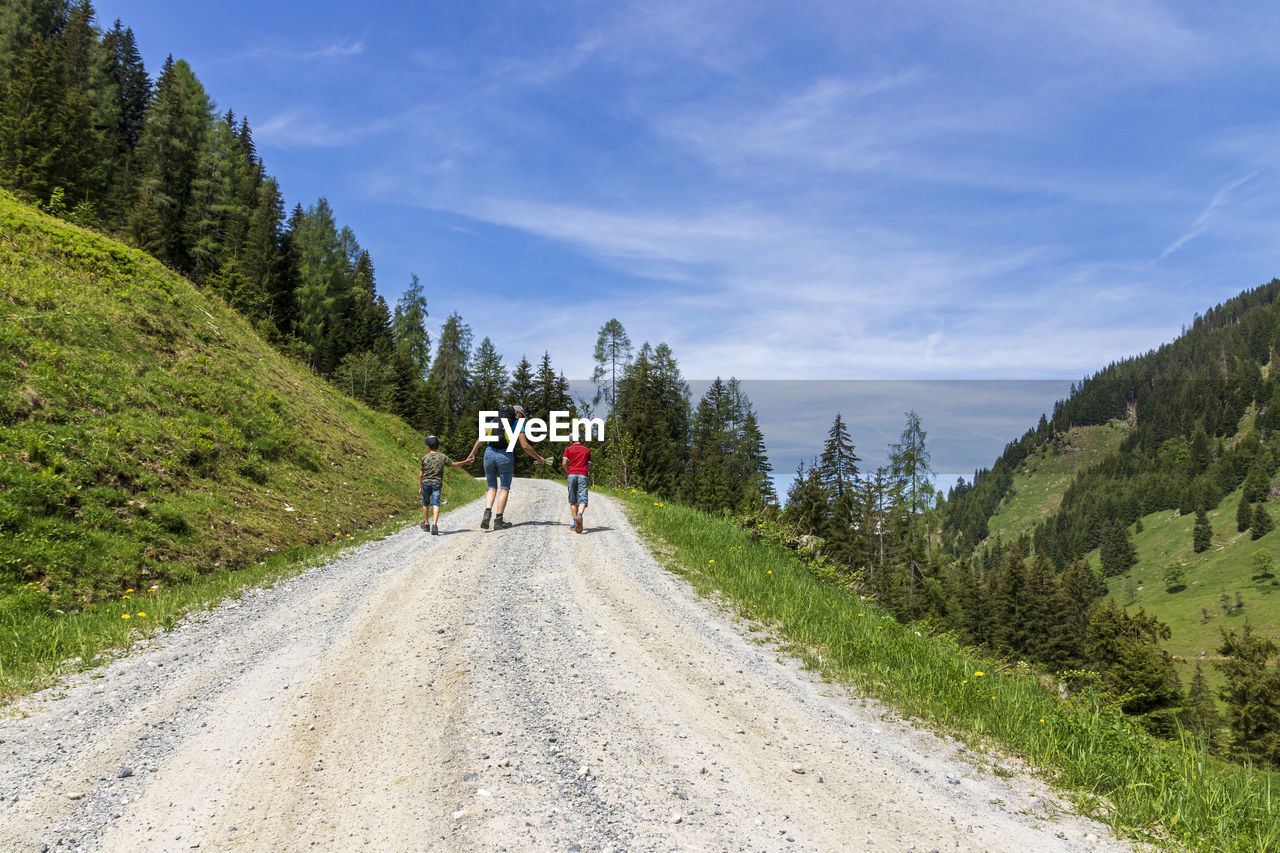 REAR VIEW OF PEOPLE RIDING MOTORCYCLE ON ROAD AGAINST TREES