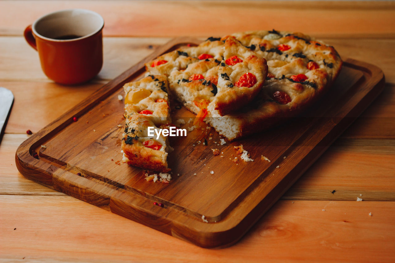 Homemade italian focaccia, with tomato and olive oil and coffee on a rustic wooden background.