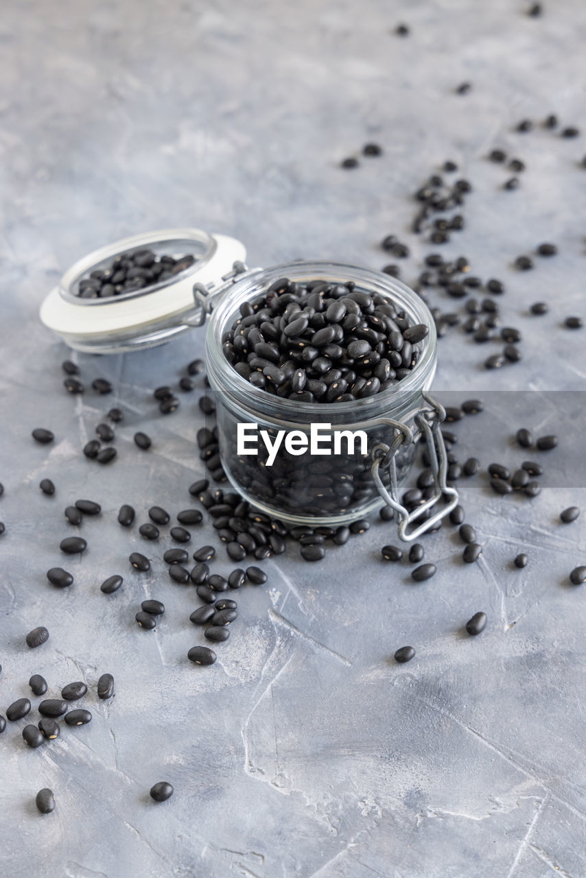 Glass jar full of dry black beans on grey table 