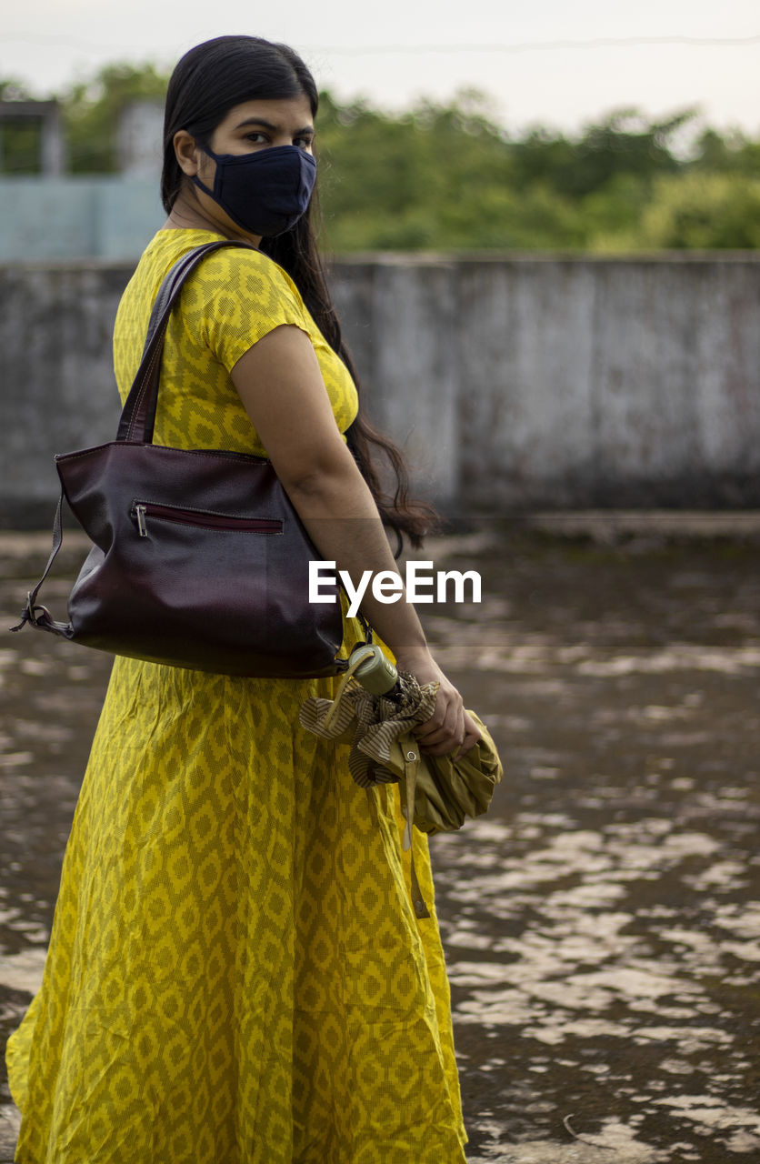 An indian woman in yellow dress and face mask on is going outside after unlock 1.0 of corona virus 