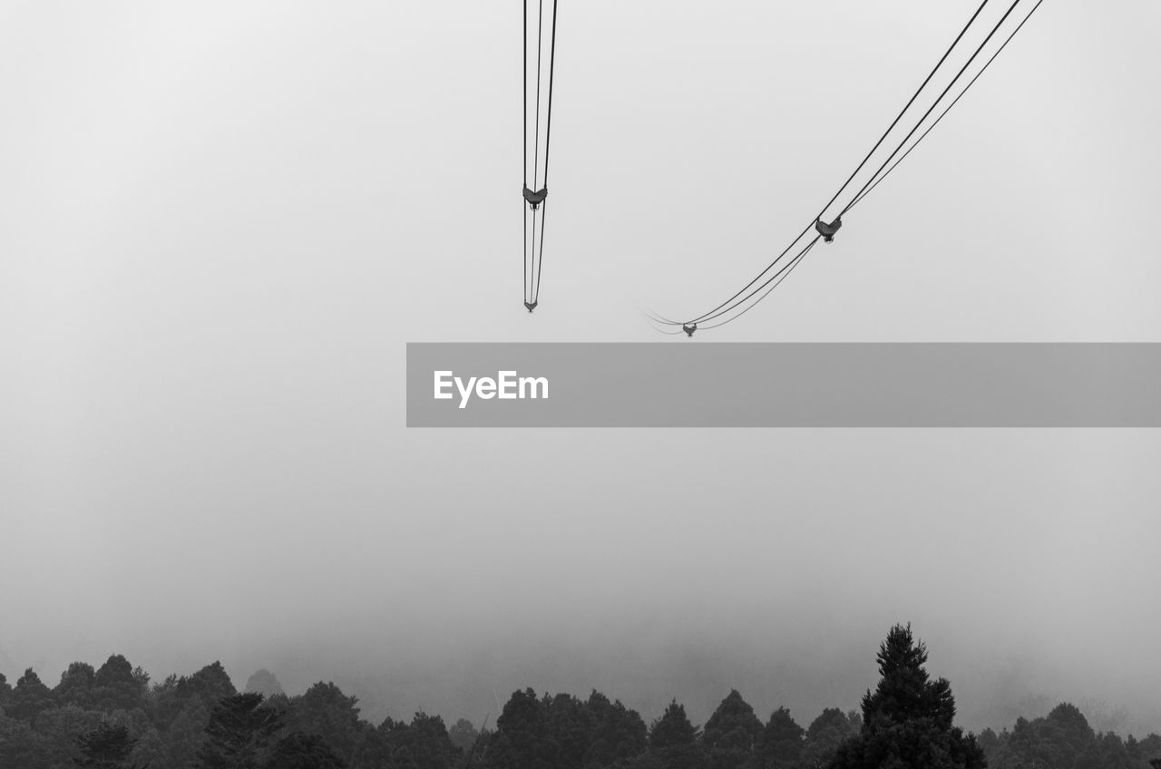 Low angle view of overhead cable car against sky during foggy weather