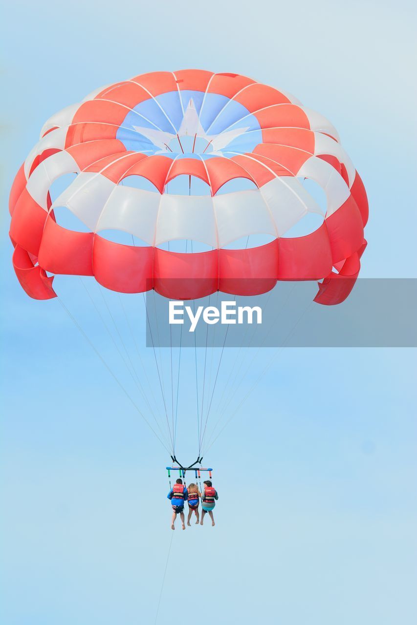 Low angle view of people parasailing against clear sky