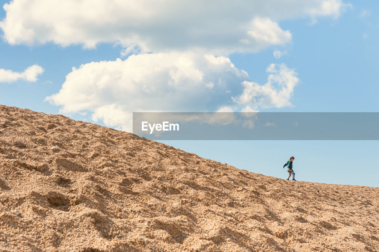 Low angle view of boy standing on sand dune against sky