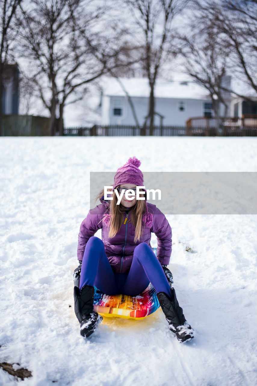 Pre teen sitting on sled in the snow in winter