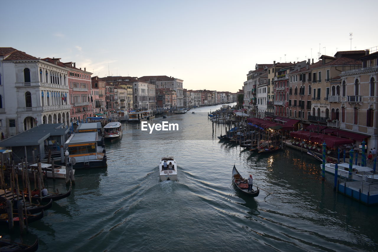 Boats in canal amidst buildings in city against sky