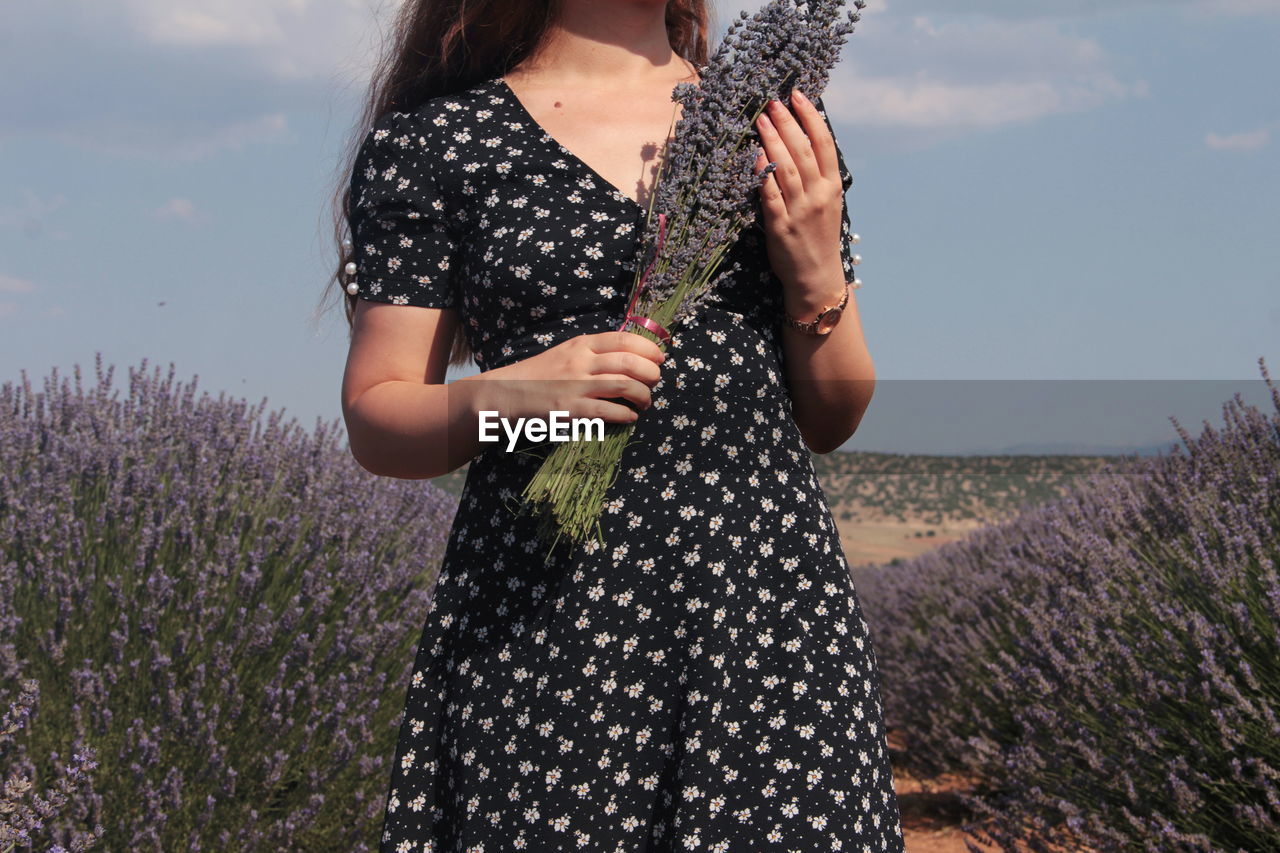 Midsection of woman standing with lavenders on field