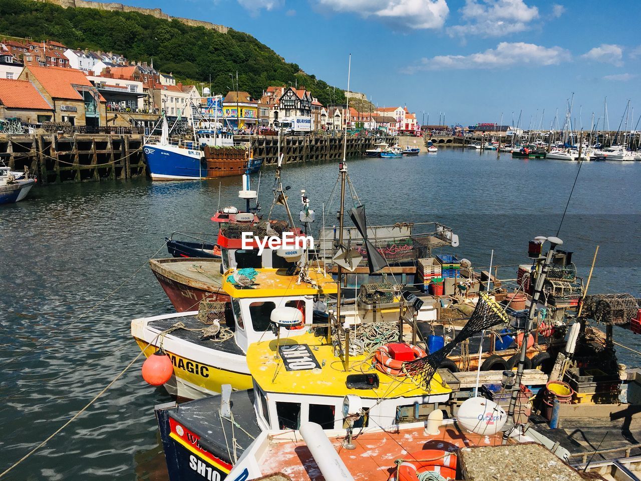 HIGH ANGLE VIEW OF FISHING BOATS MOORED AT HARBOR BY BUILDINGS