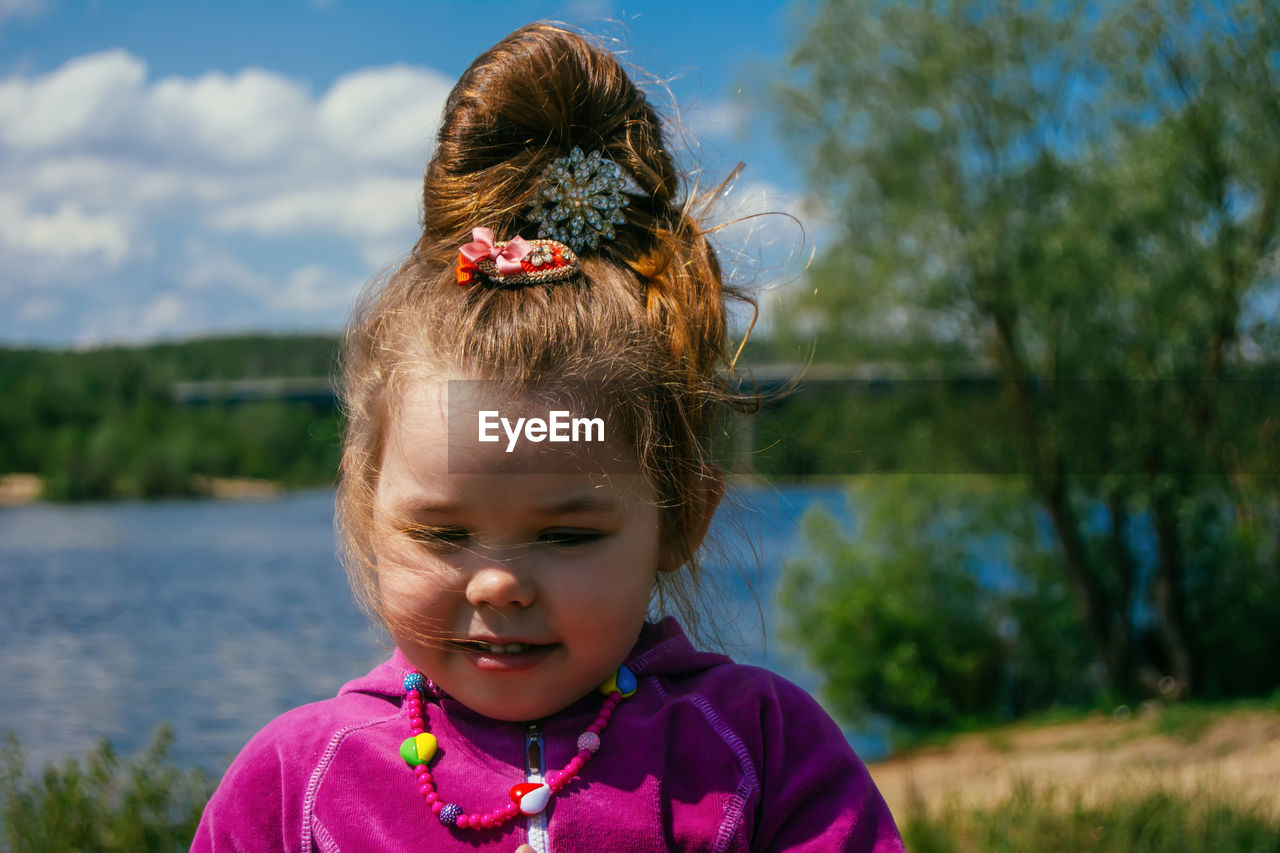 Cute girl with hair bun against lake during summer