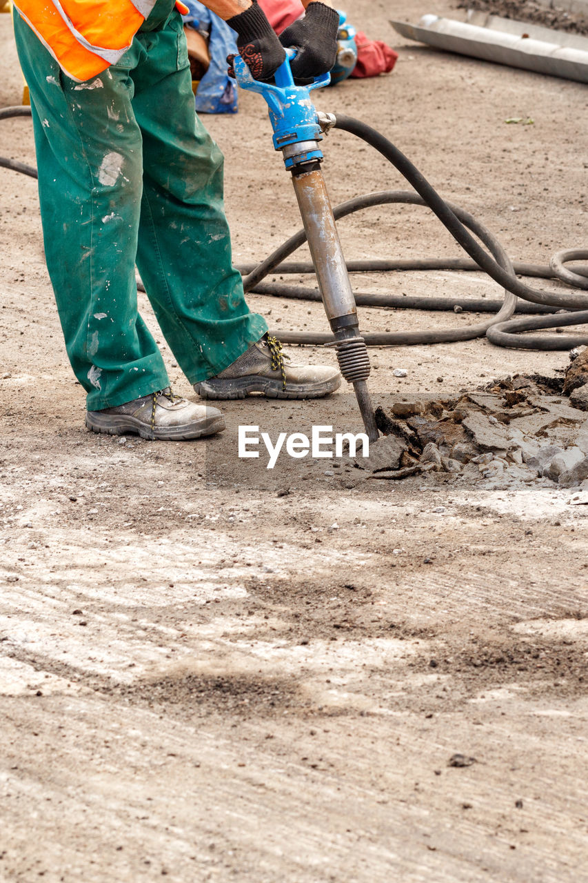 A road worker smashes old asphalt with a pneumatic jackhammer at a work site.