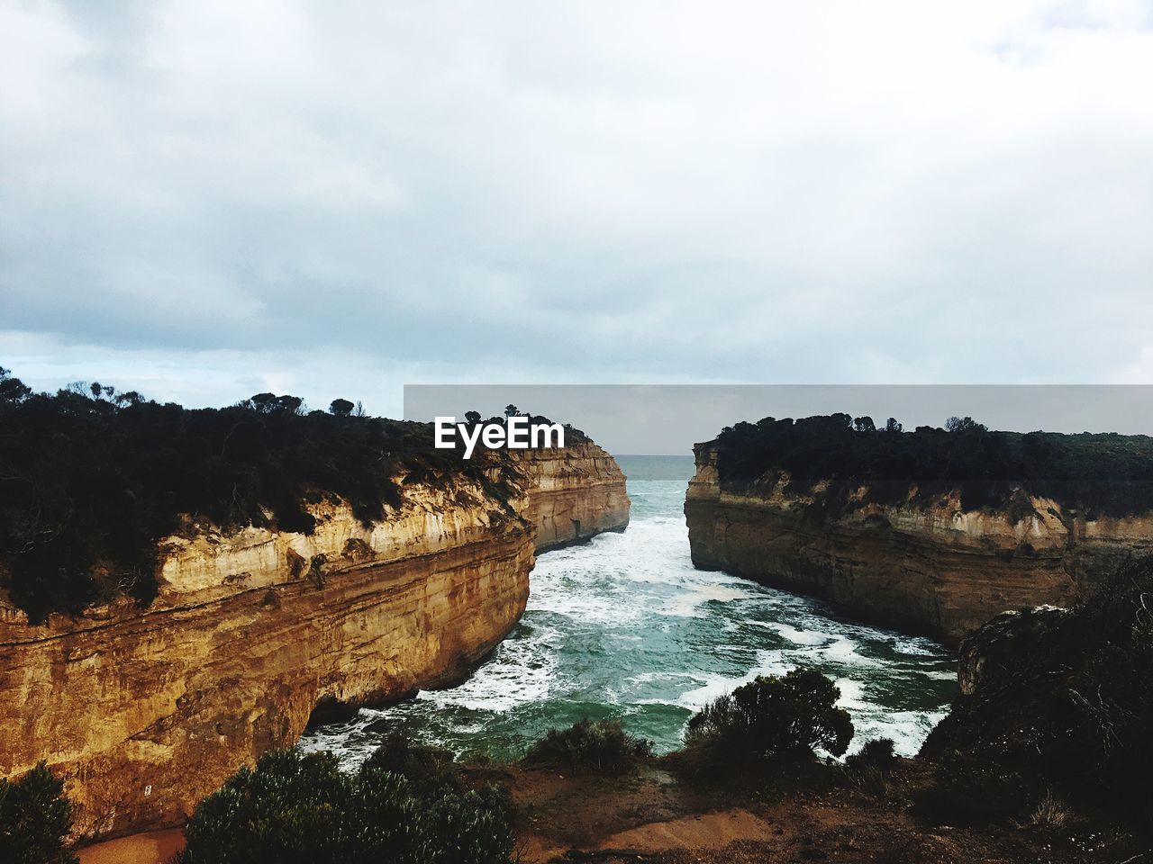 Rock formations by sea against cloudy sky