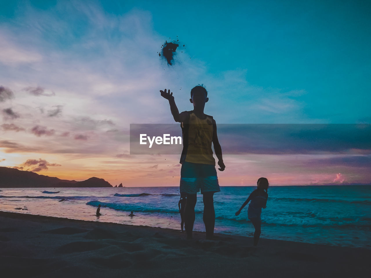 Man throwing sands while standing at beach during sunset