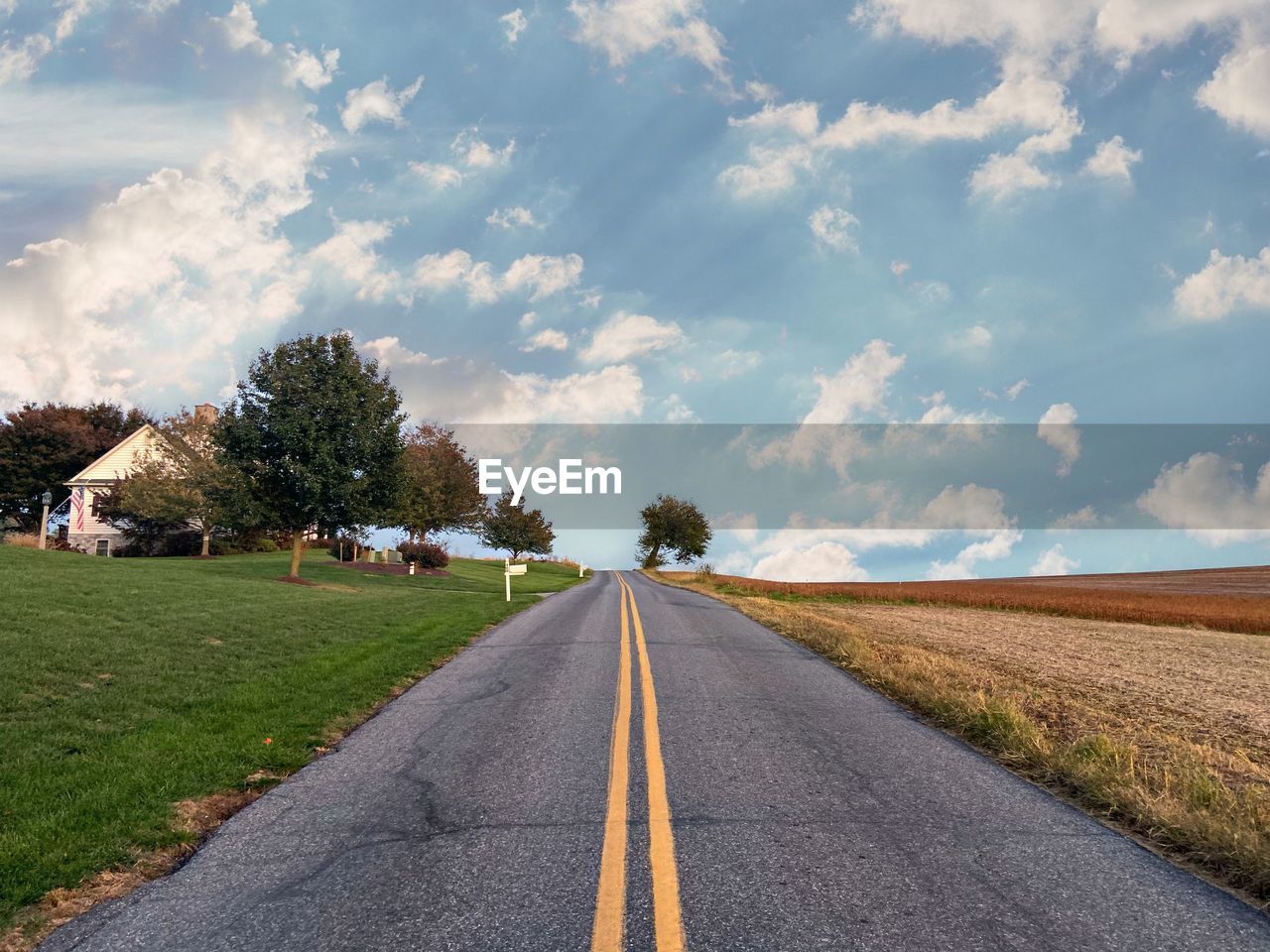 Empty road amidst field against sky