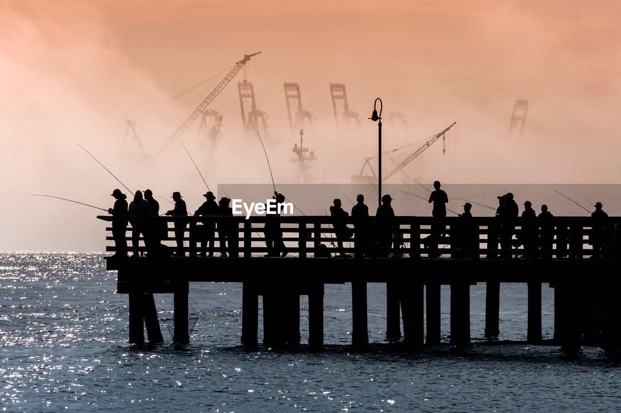 Silhouette people on pier by sea against sky during sunrise