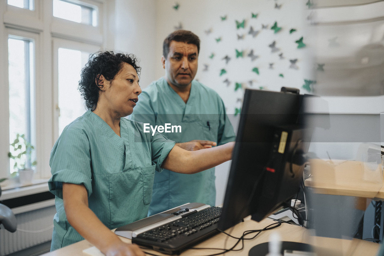 Male and female healthcare workers discussing over computer at reception desk in hospital