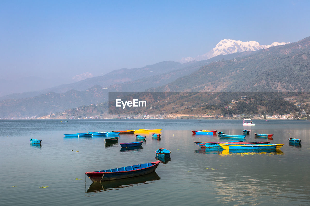 Boats moored on sea against clear blue sky