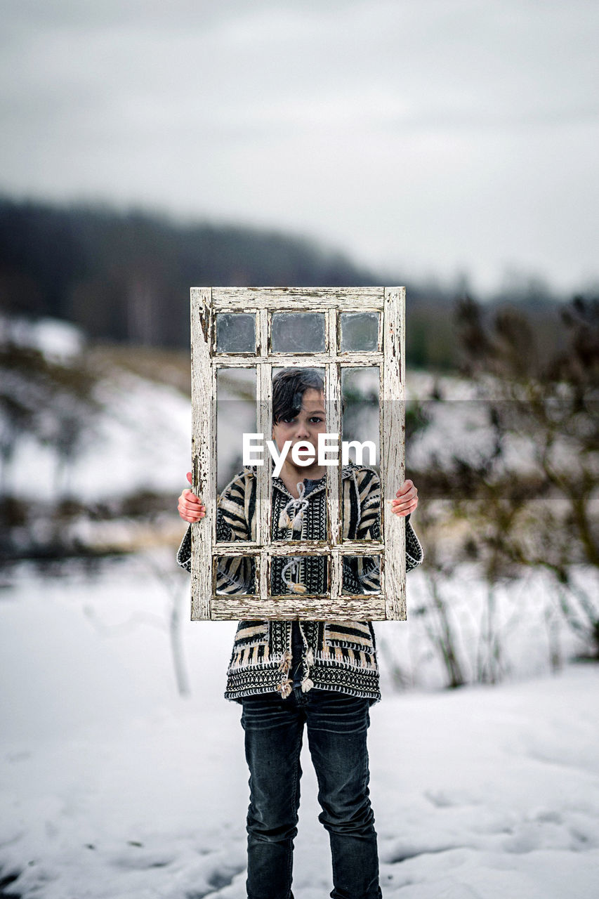 Low section of kid standing on snow holding window frame