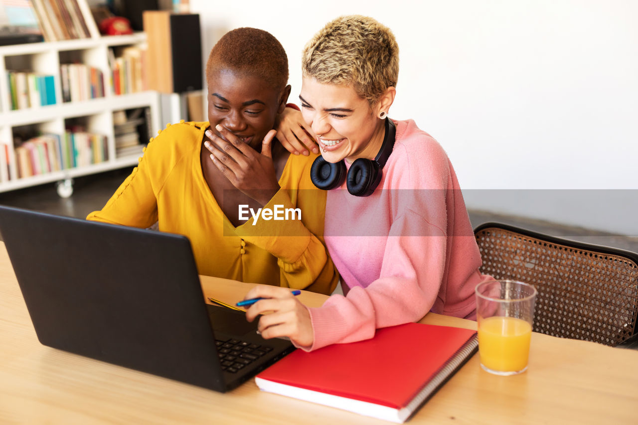 Cheerful lesbian couple using laptop on table at home