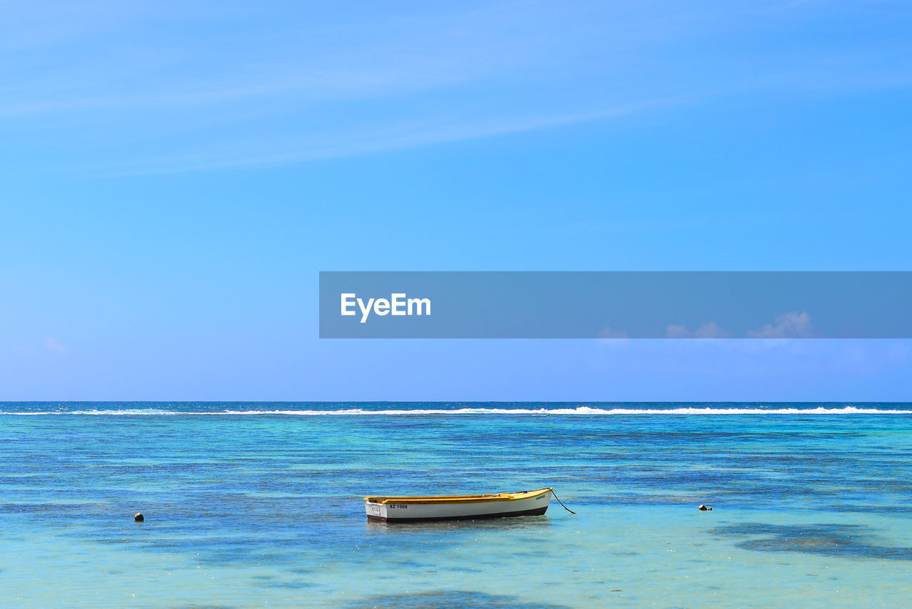 Boat anchored at beach against blue sky