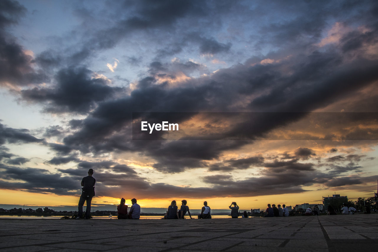 People at beach against cloudy sky during sunset