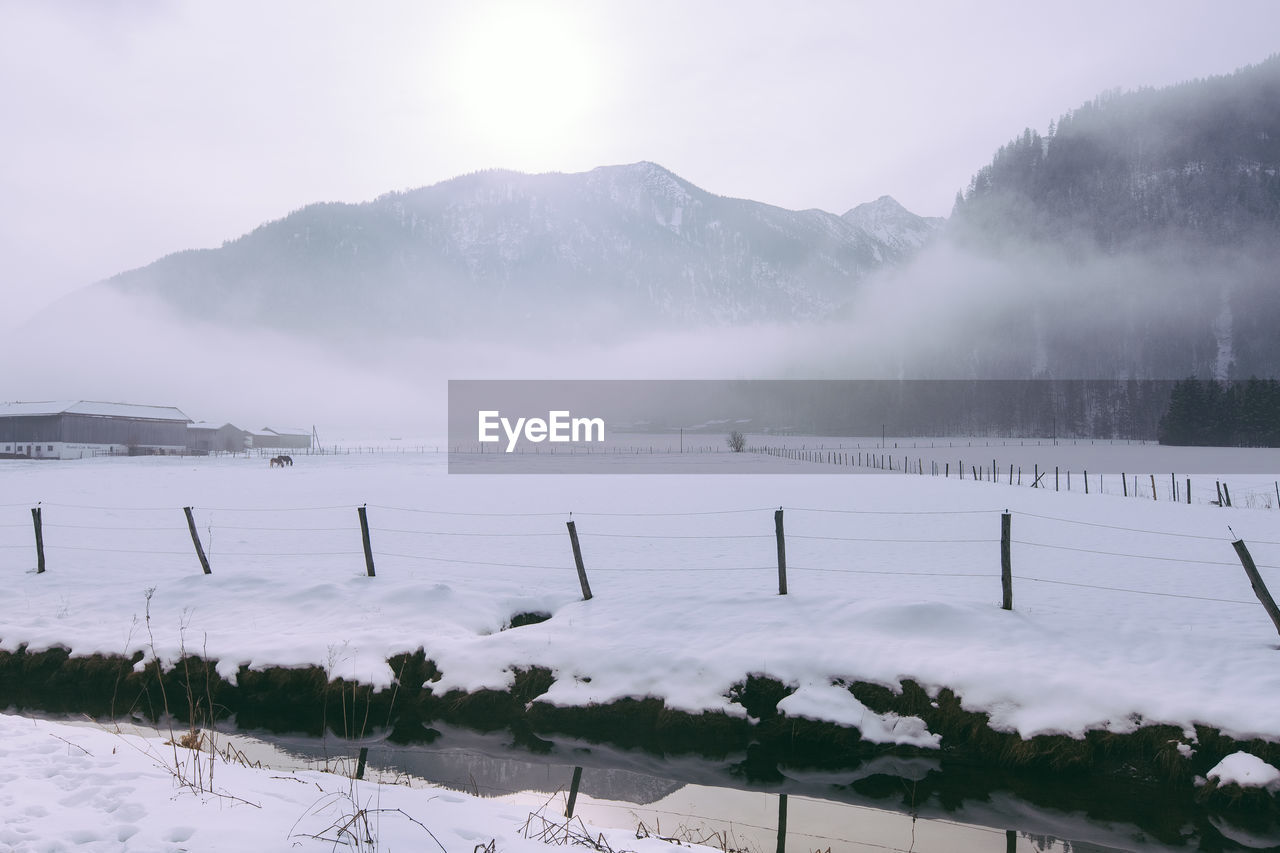 Fence on snow covered field against mountain