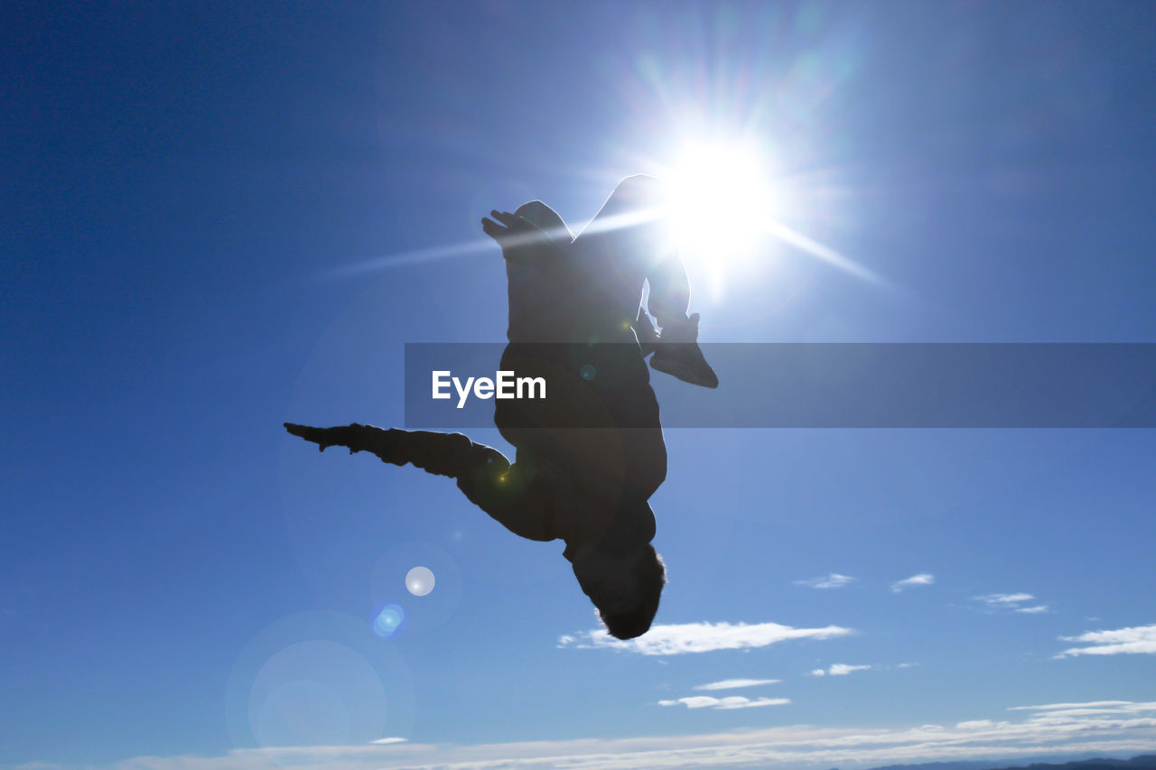 Low angle view of silhouette man jumping with sun shining in sky