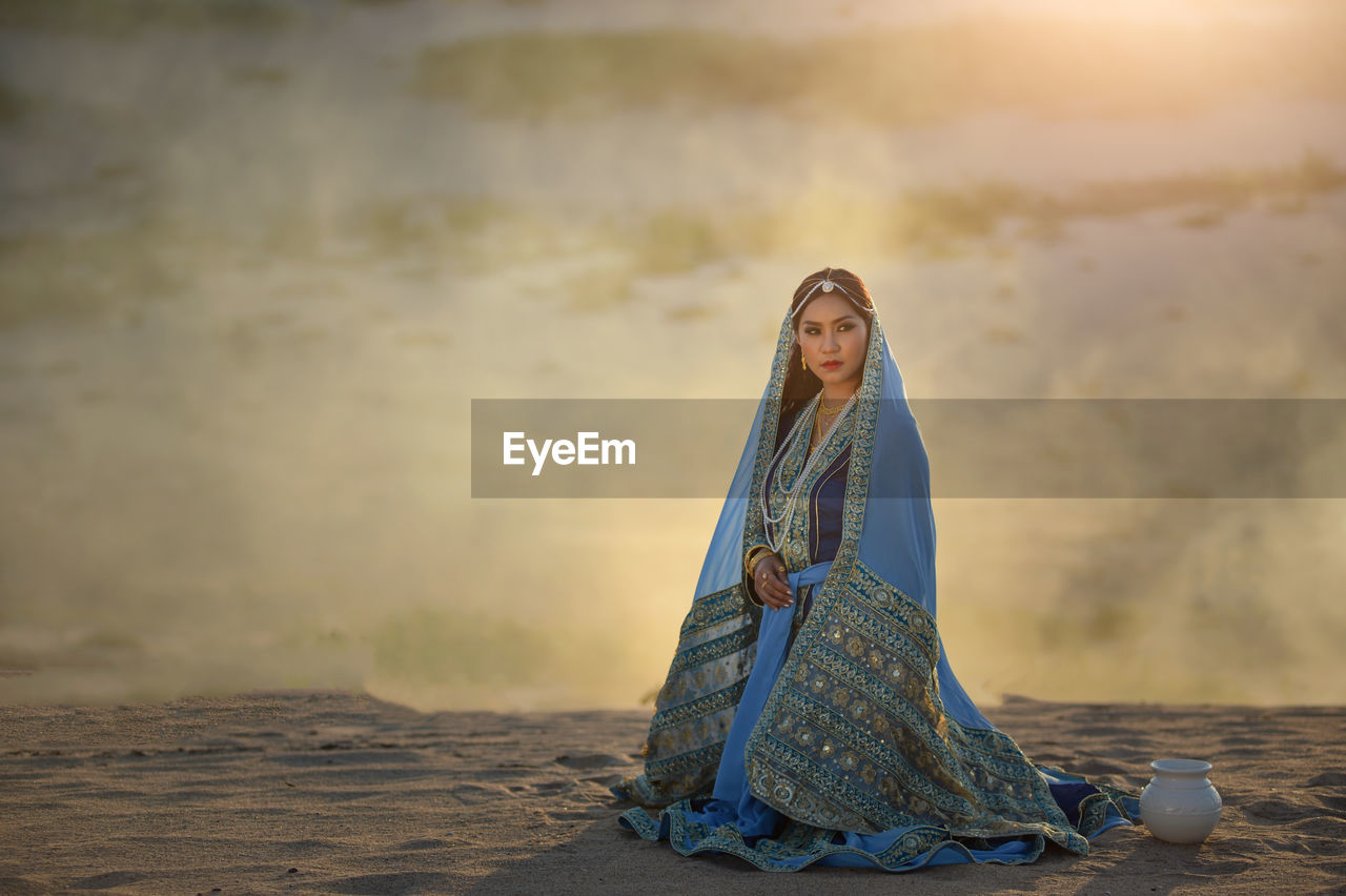 Young woman wearing traditional clothing kneeling on land