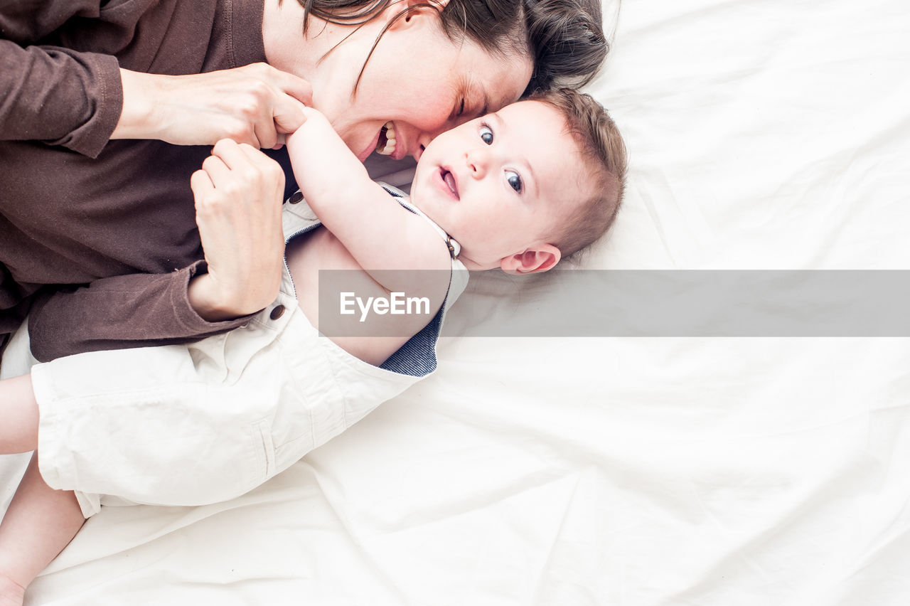 HIGH ANGLE VIEW OF MOTHER LYING ON BED