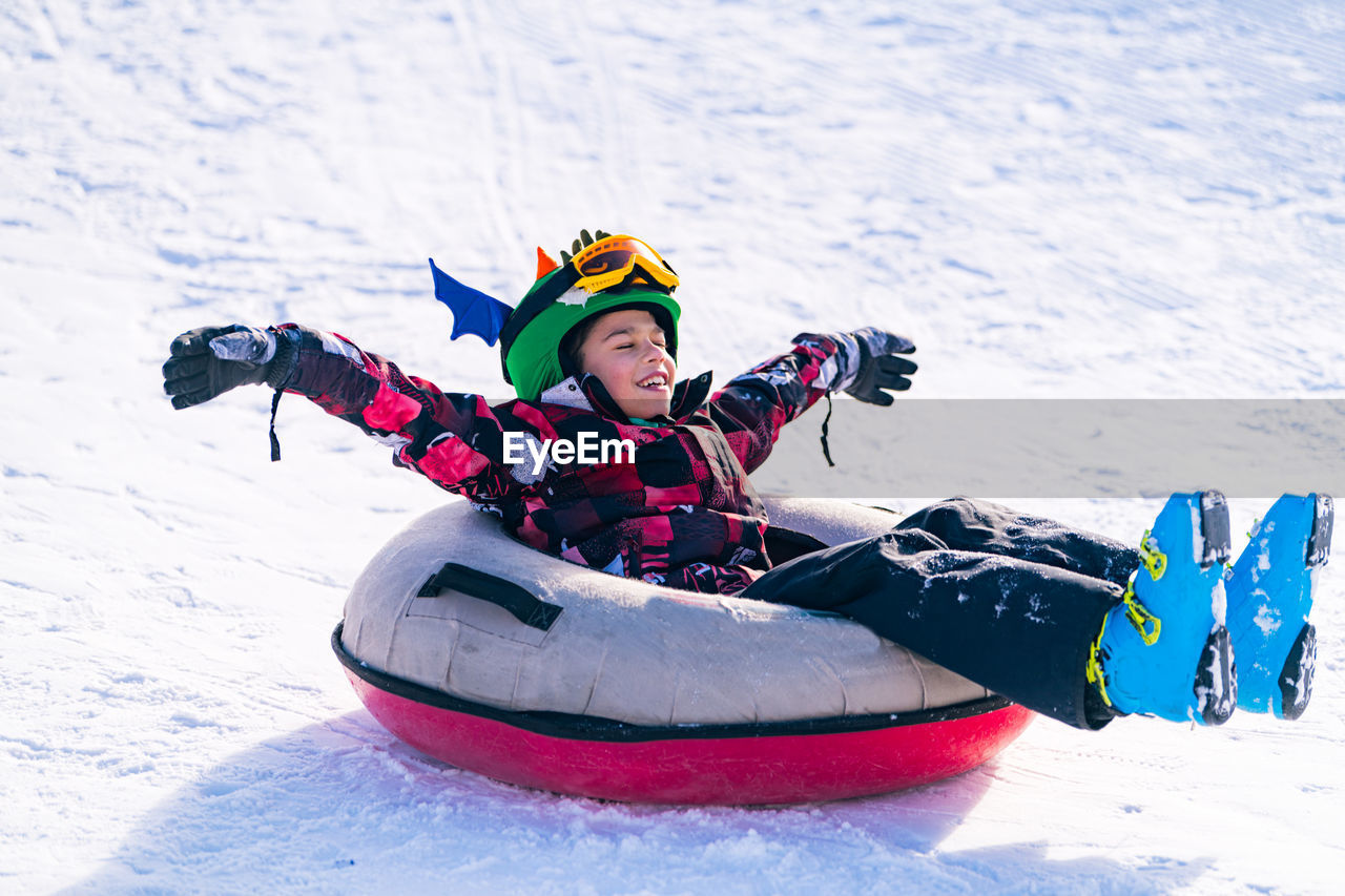 Full length of boy over inflatable raft on snow