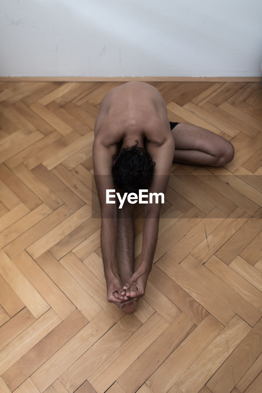 High angle view of man lying on floor at home doing yoga