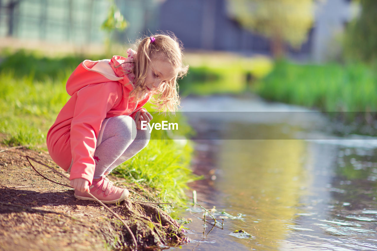 Girl holding stick while crouching by canal