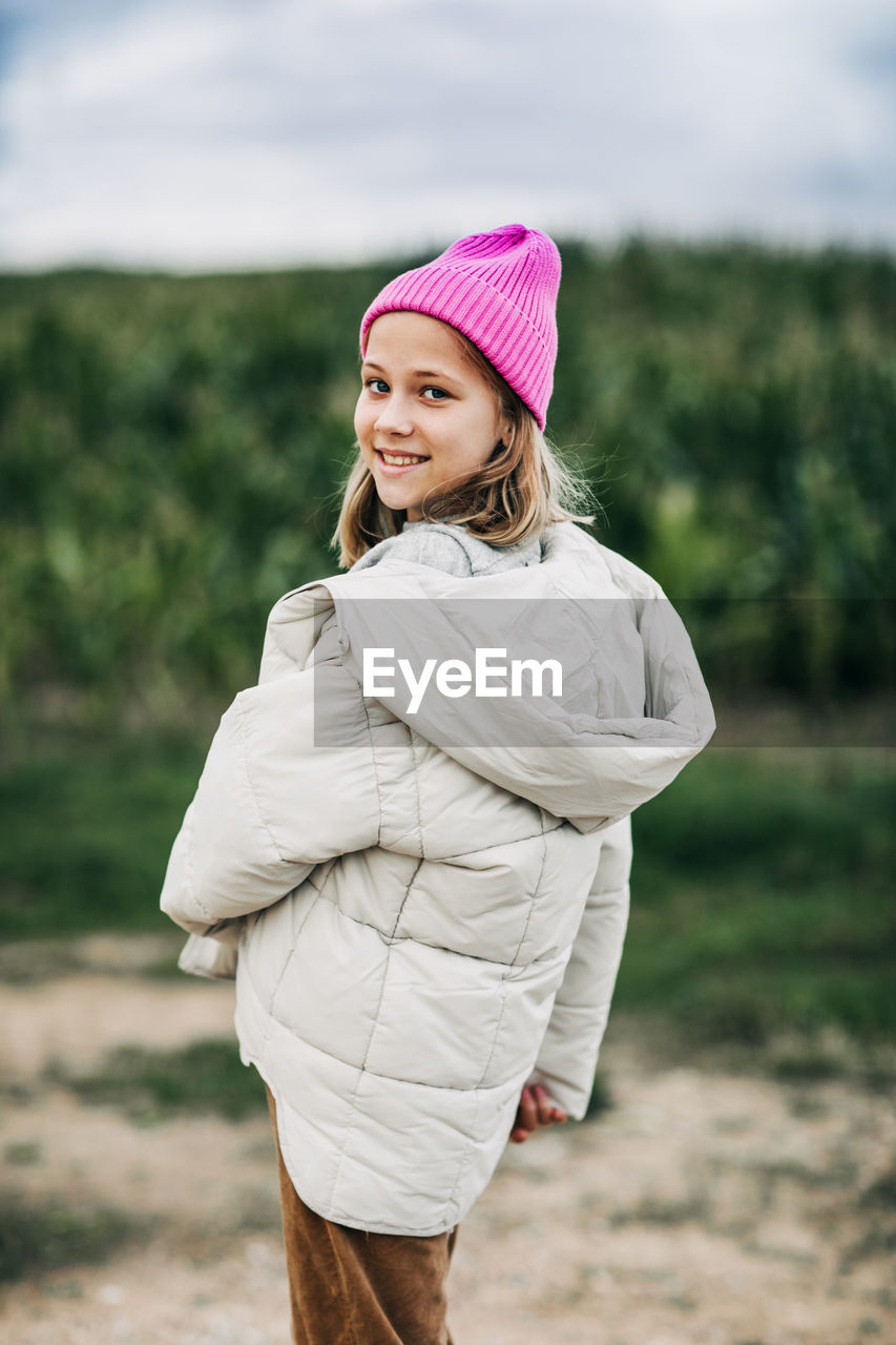 Cheerful beautiful teenage girl in a yellow raincoat and a pink hat is dancing on the background 