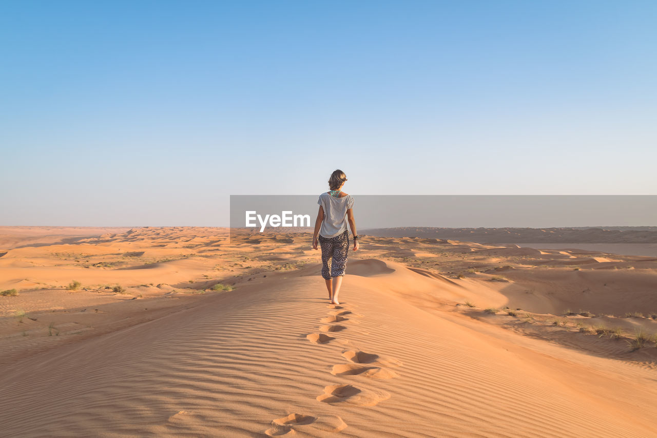 Rear view full length of woman walking at desert against clear sky