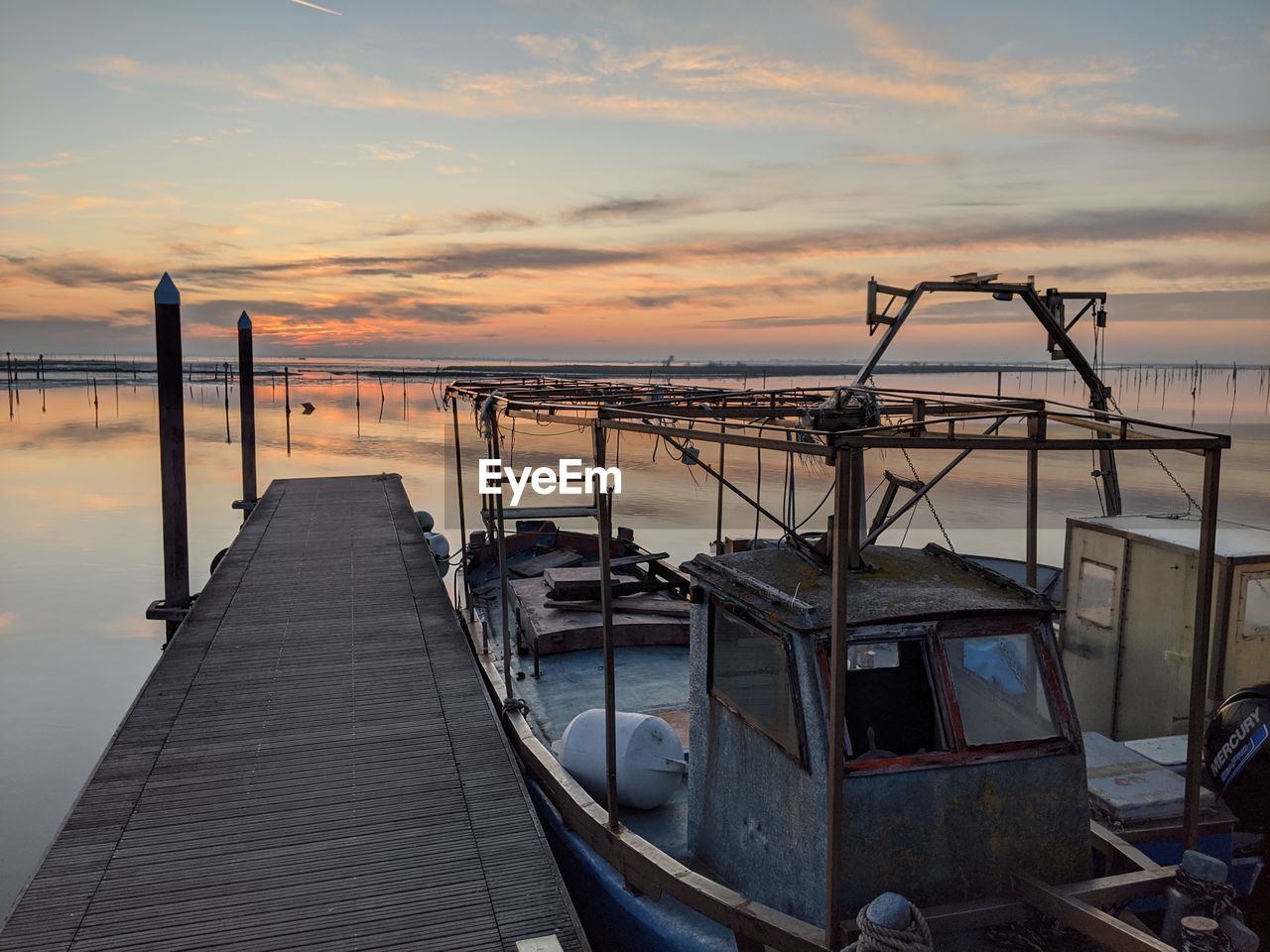 Pier and sailboat over sea against sky during sunset