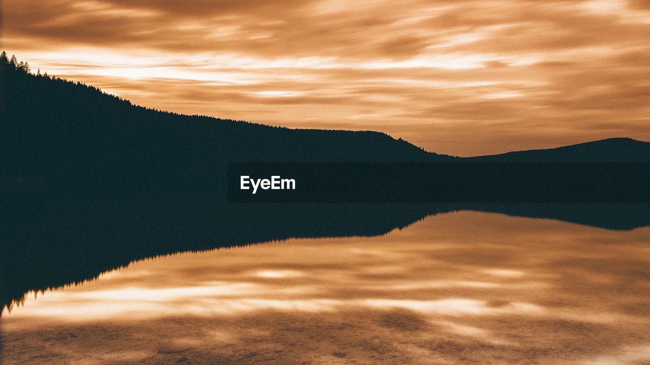 Scenic view of lake by mountains against sky during sunset