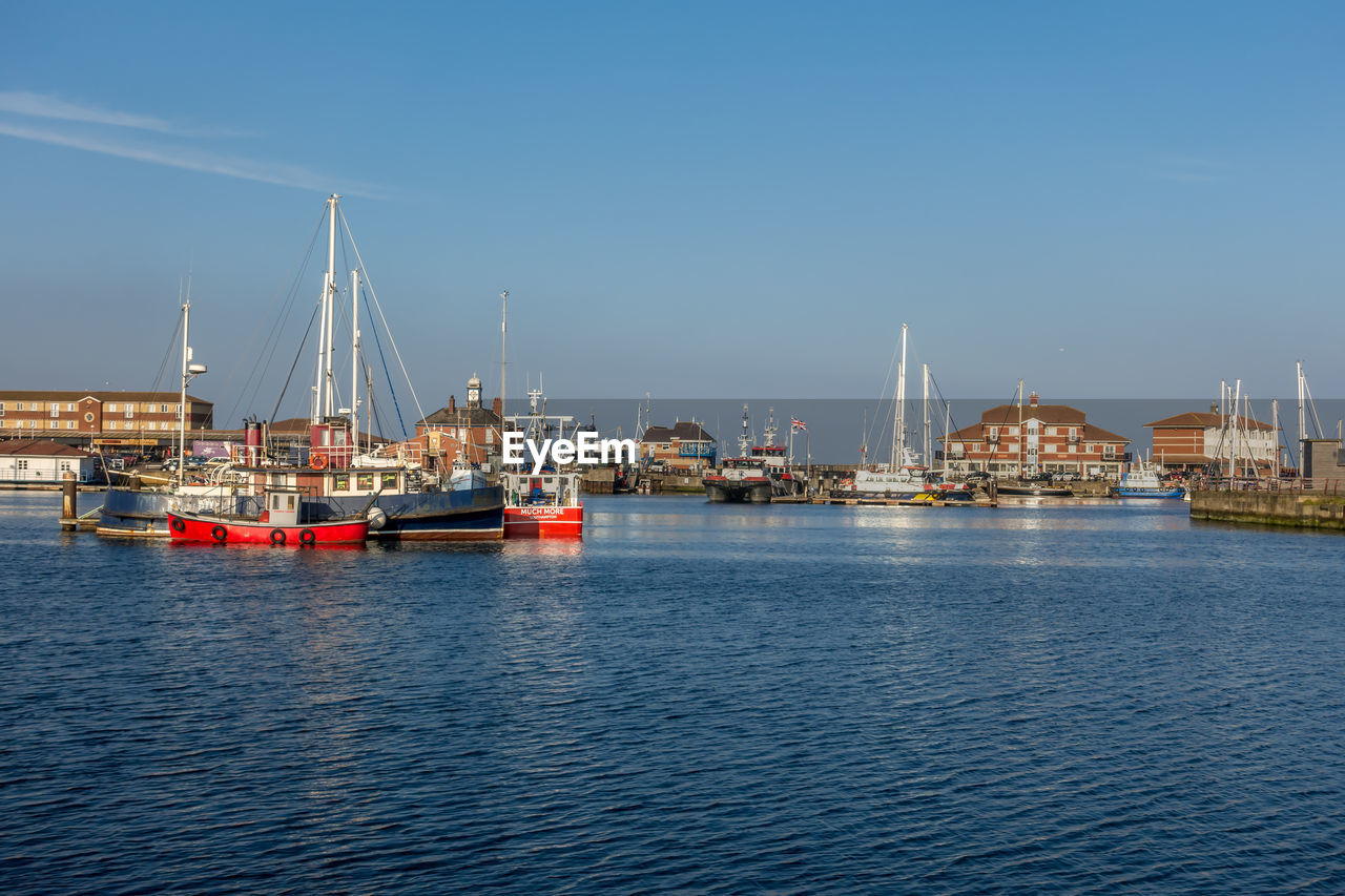 SAILBOATS IN SEA BY HARBOR AGAINST SKY