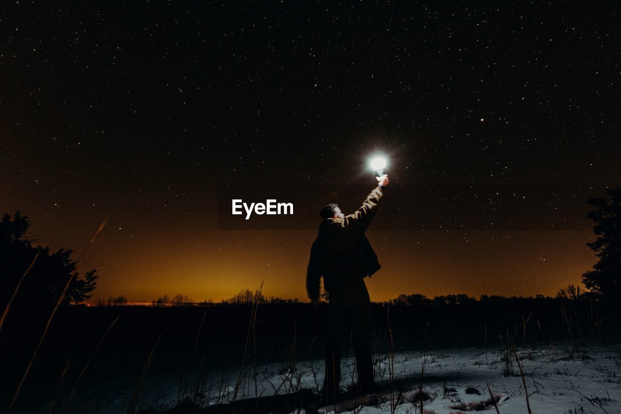 Silhouette man standing on snow against sky at night