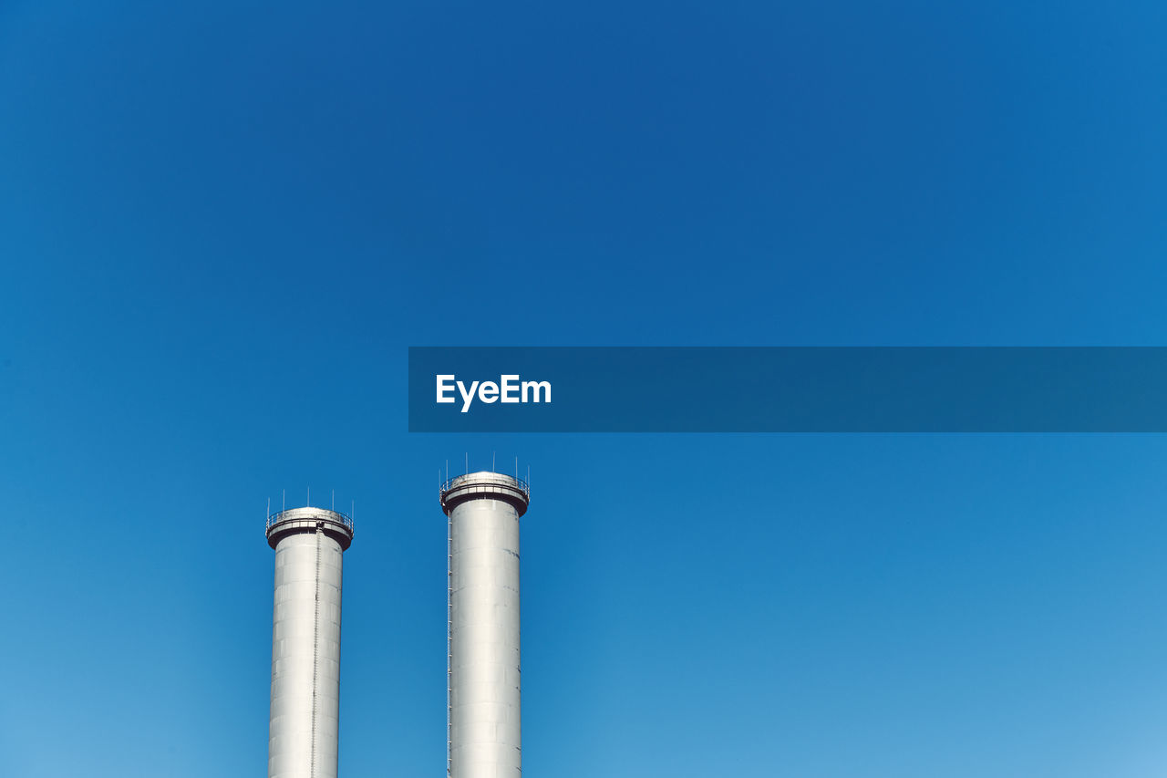 Low angle view of smoke stacks against blue sky