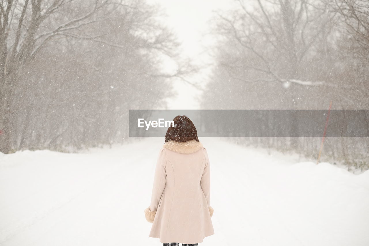 Rear view of woman walking on snow covered field