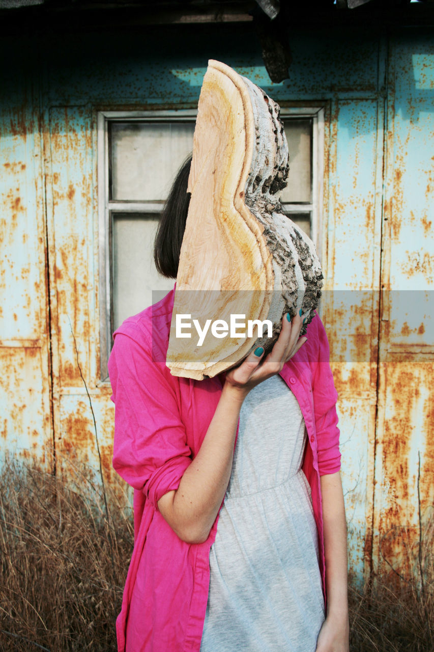 Woman holding wood while standing against wall