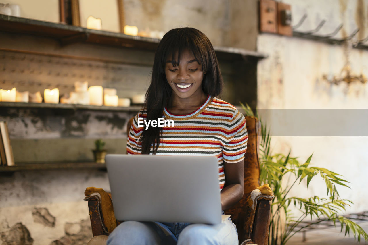 Portrait of smiling young woman sitting on leather chair using laptop