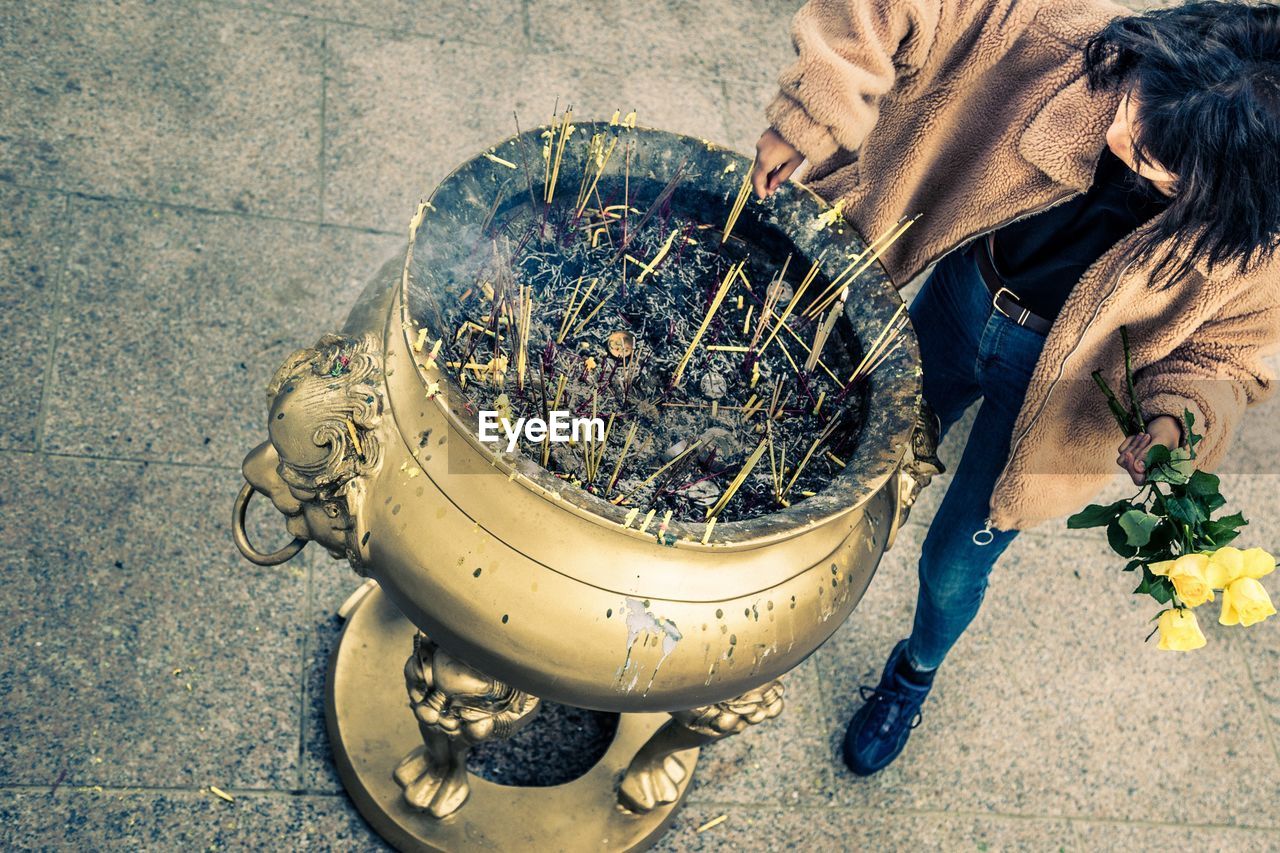 High angle view of girl holding yellow roses while standing by incense in pot at temple