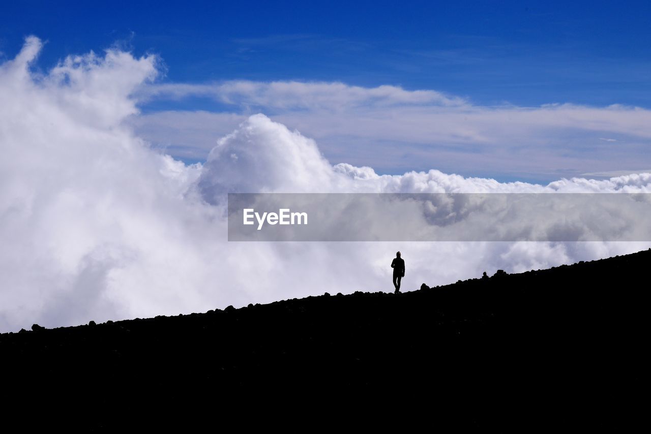 Silhouette person on hill against cloudy sky