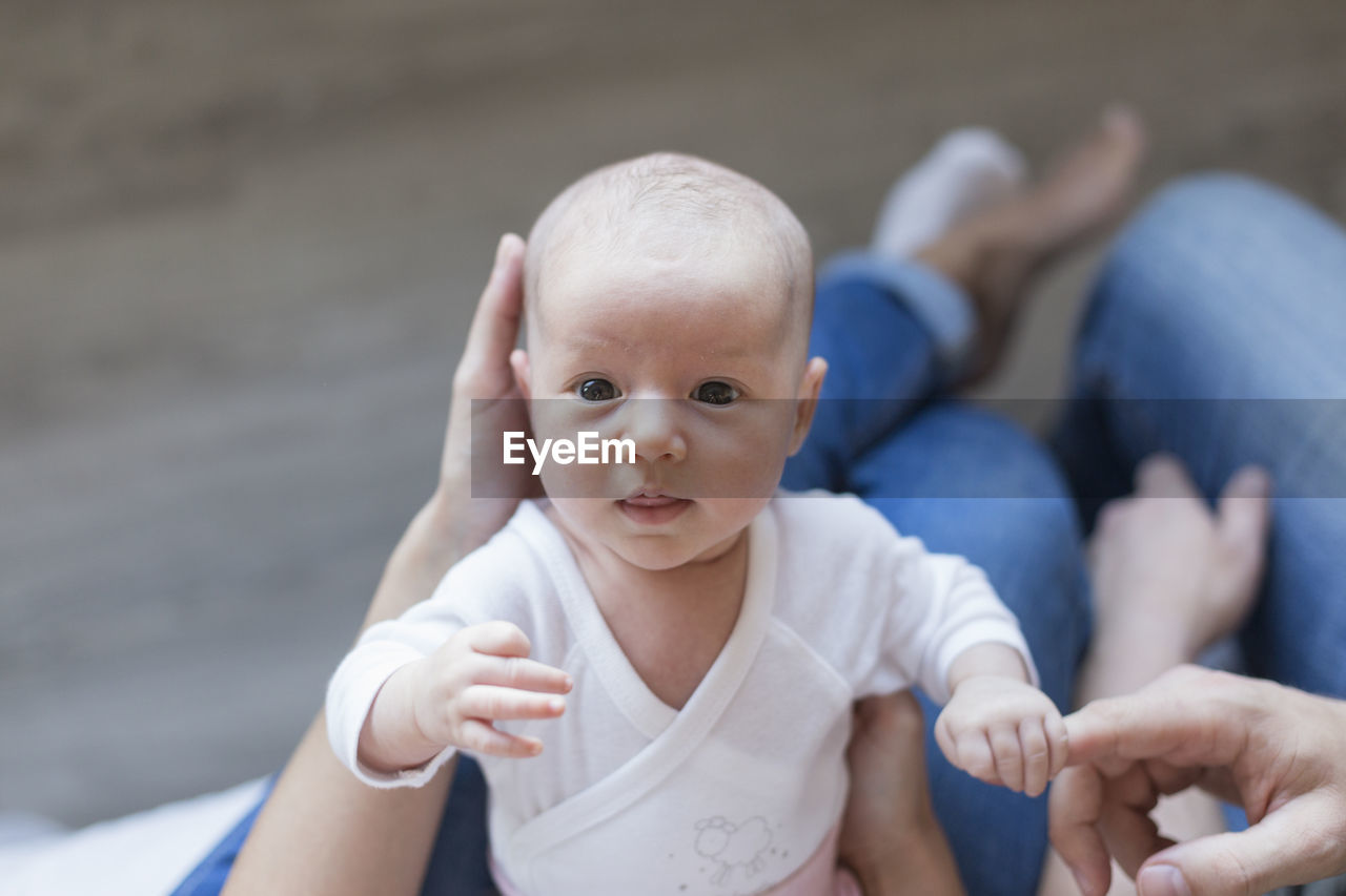 Low section woman holding cute baby girl sitting on floor at home