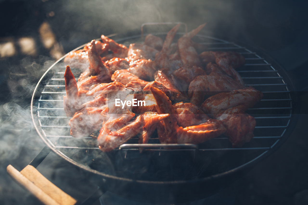   chicken wings lie on a steaming barbecue grill.