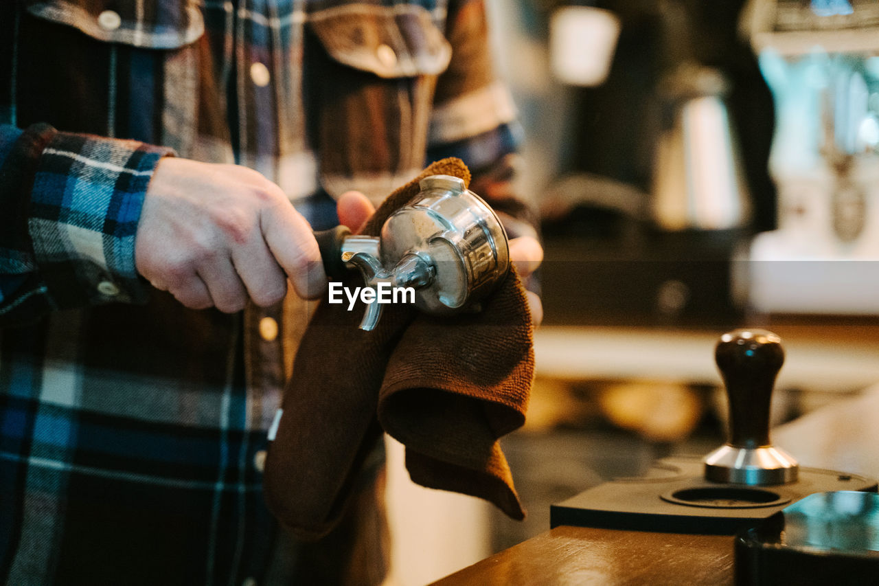 Anonymous crop male barista with portafilter preparing beverage in contemporary coffee machine while working in cafe