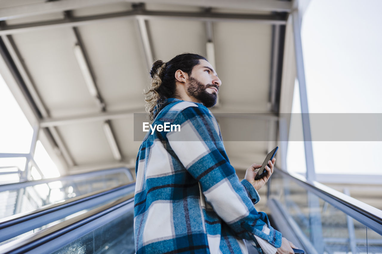 Young man using mobile phone while standing on escalator