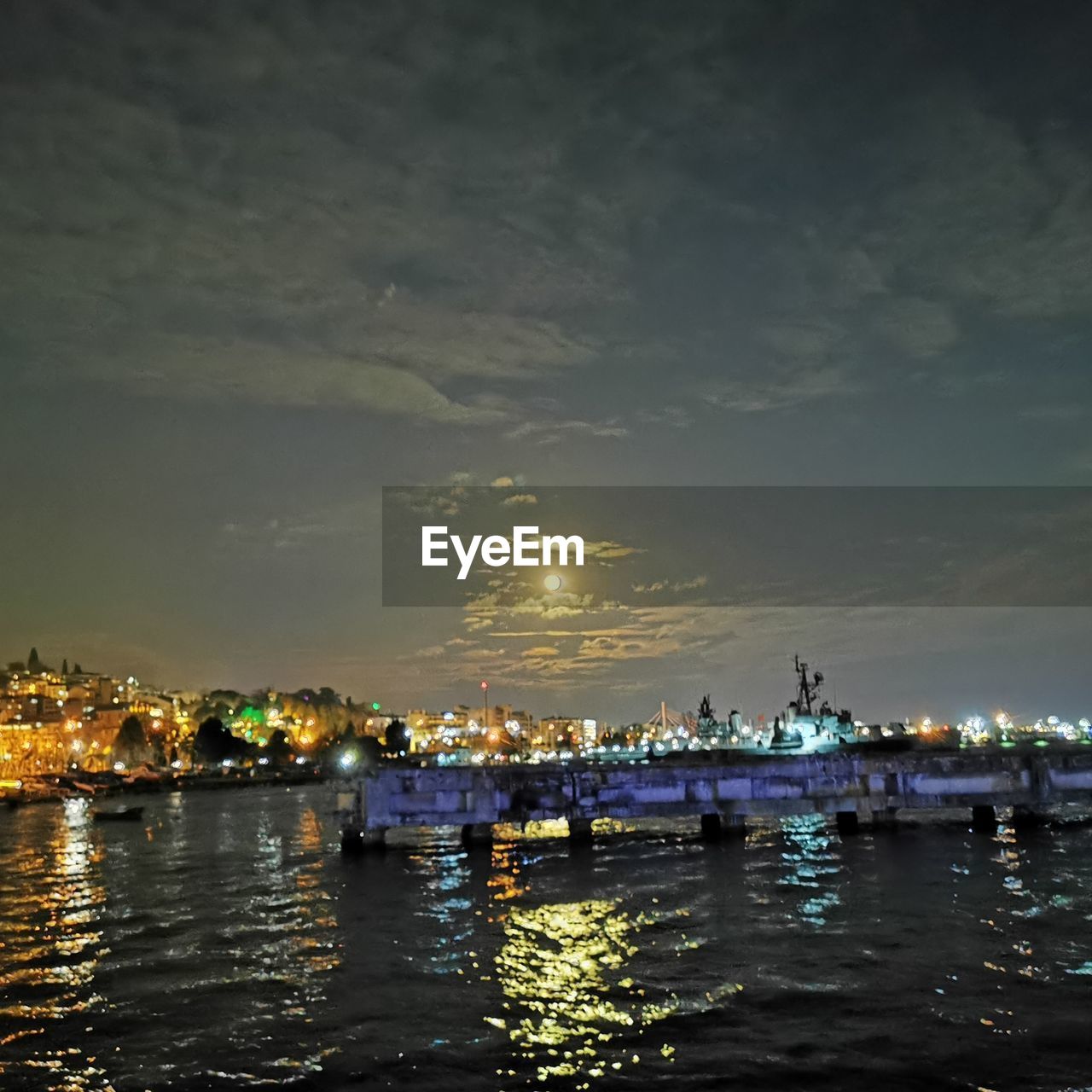 ILLUMINATED BUILDINGS BY SEA AGAINST SKY AT NIGHT IN CITY