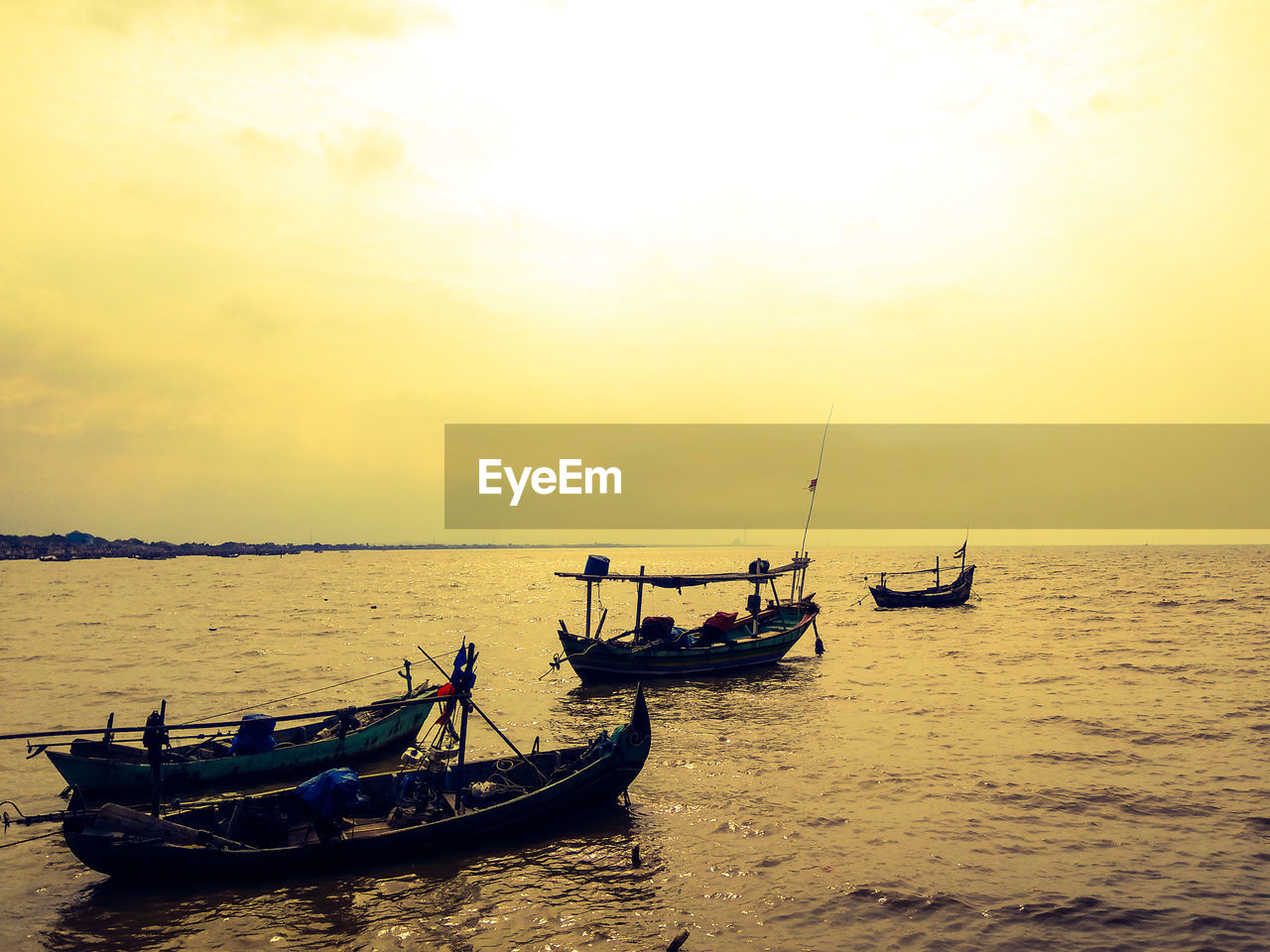 Boats moored in sea against sky during sunset